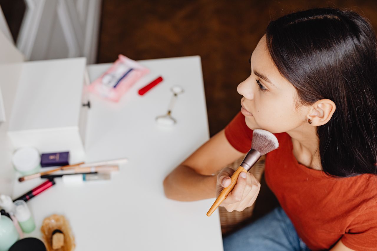 Top view of a woman applying makeup with a brush at a vanity table.